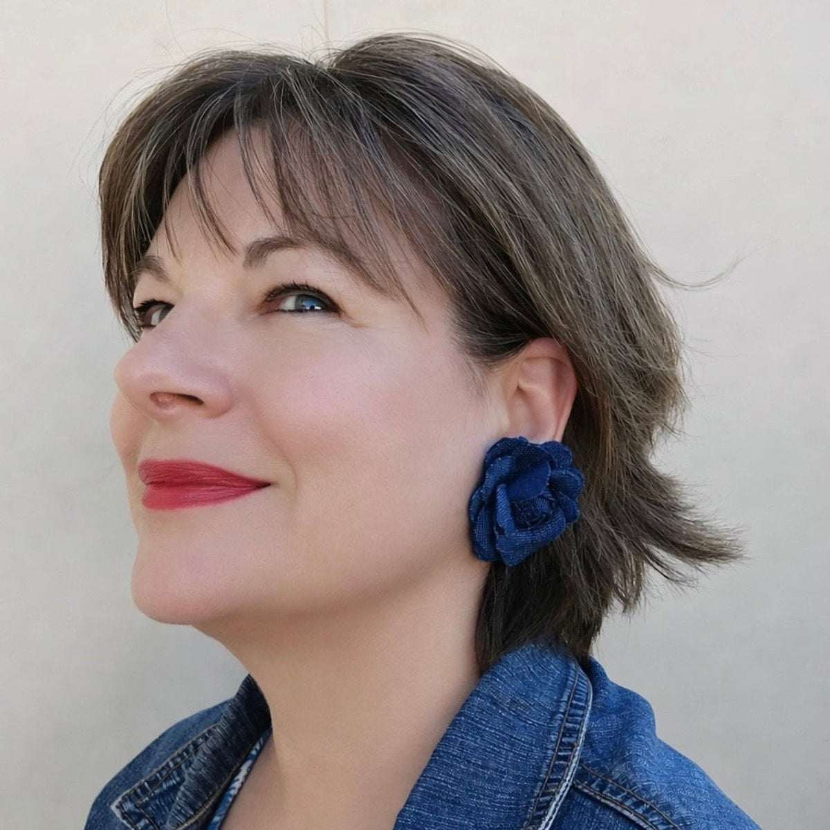 Woman wearing blue floral earrings against a plain background