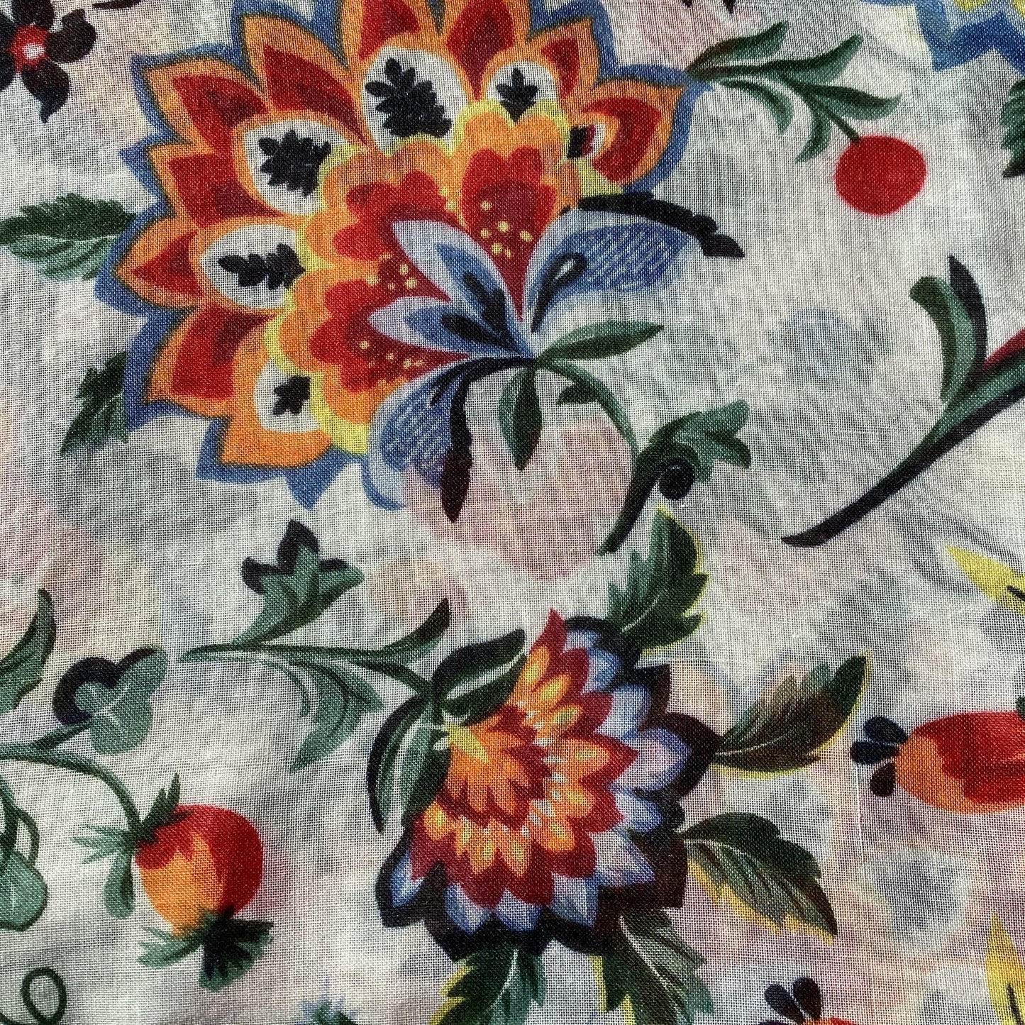 a close up picture of a ladies scarf that has a white background and bright red, orange, denim blue and green leaves design