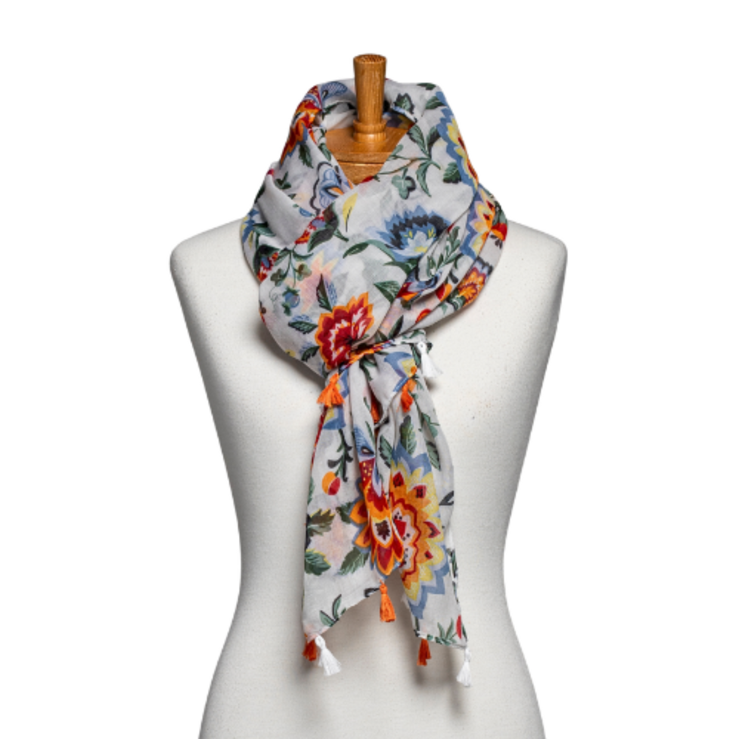 a ladies scarf that is tied around the neck of a mannequin. The scarf has a white background and bright red and orange flowers, blue and green foliage and is finished with alternating orange and white tassels