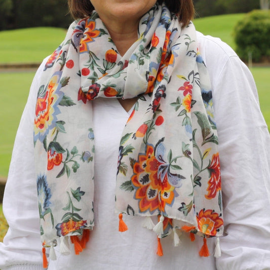 a lady wearing a pretty scarf that has a white background, organge, blue and sage green flowers and orange and white tassels