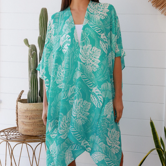 Woman wearing a teal floral kimono in a room with plants and a white wall.