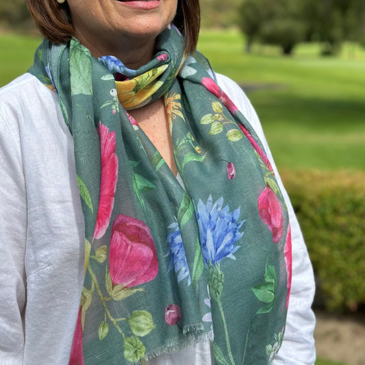 a lady wearing a dark green scarf with large flowers of pink, blue, yellow with green leaves