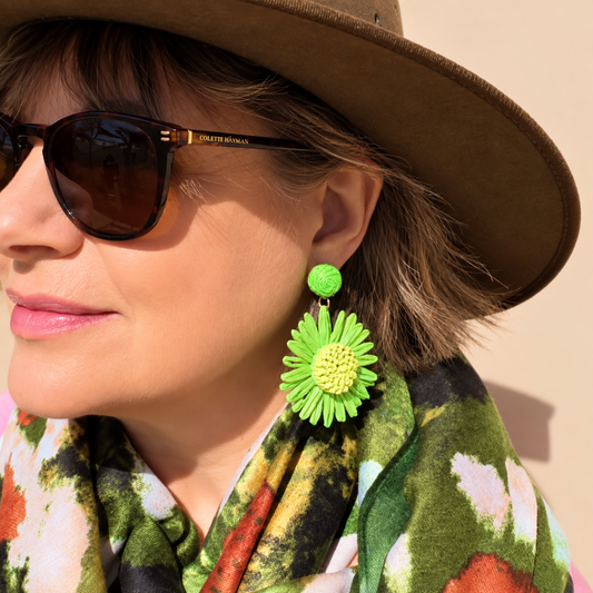 a woman wearing a hat, sunglasses and line green flower earrings with a green scarf