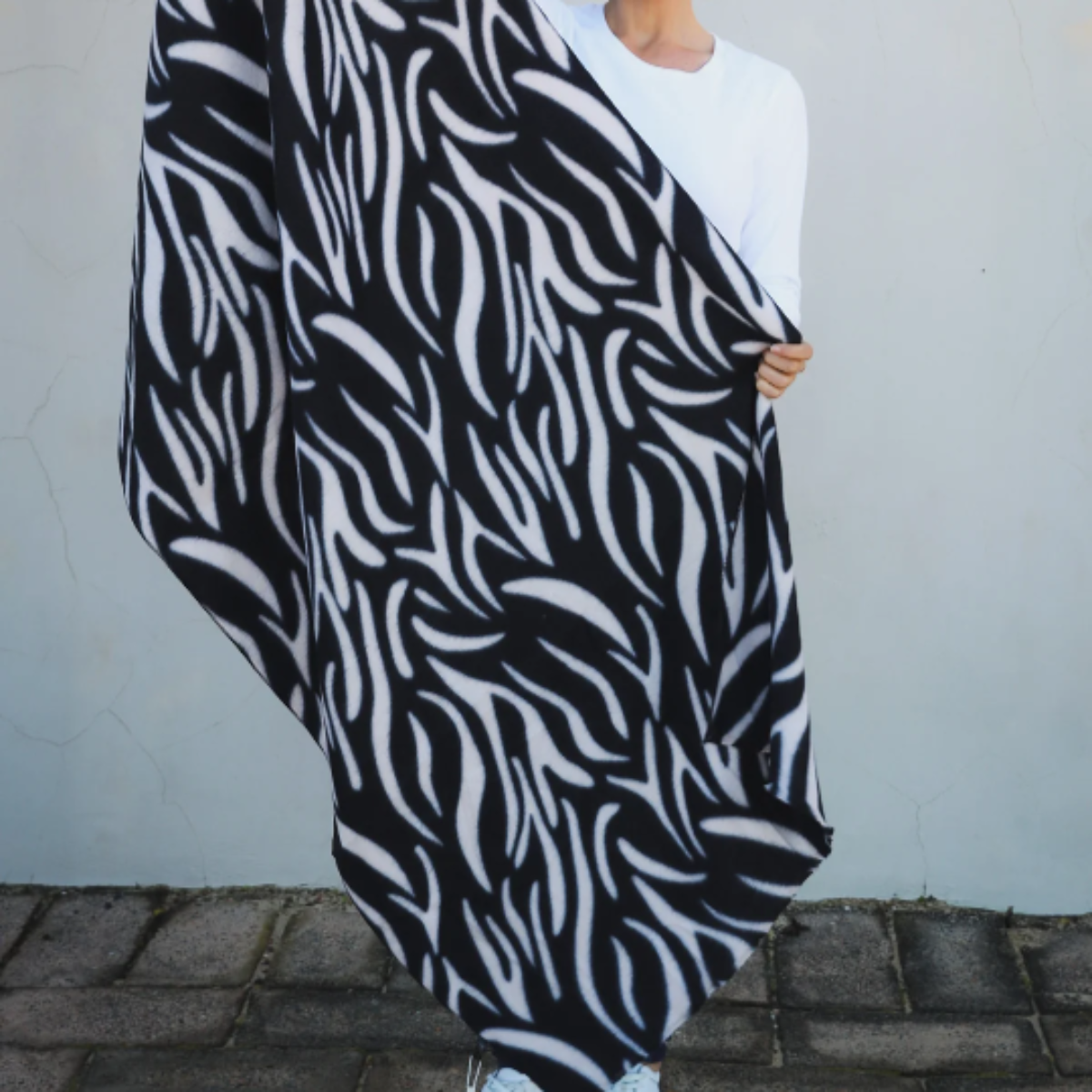 Lady holding a large black and white patterned scarf against a light-colored wall.