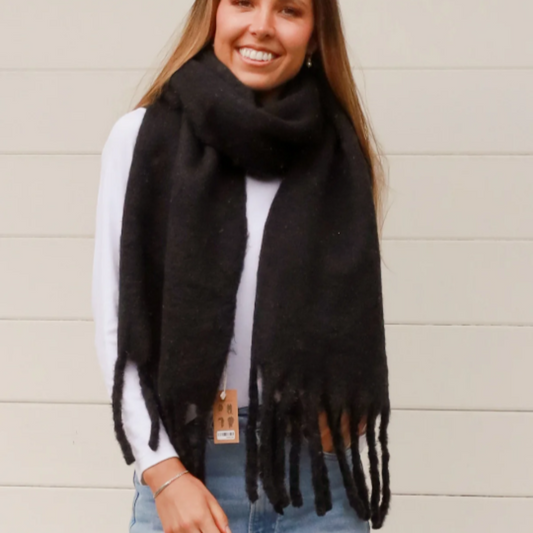 Woman wearing a black scarf with fringes against a beige wall