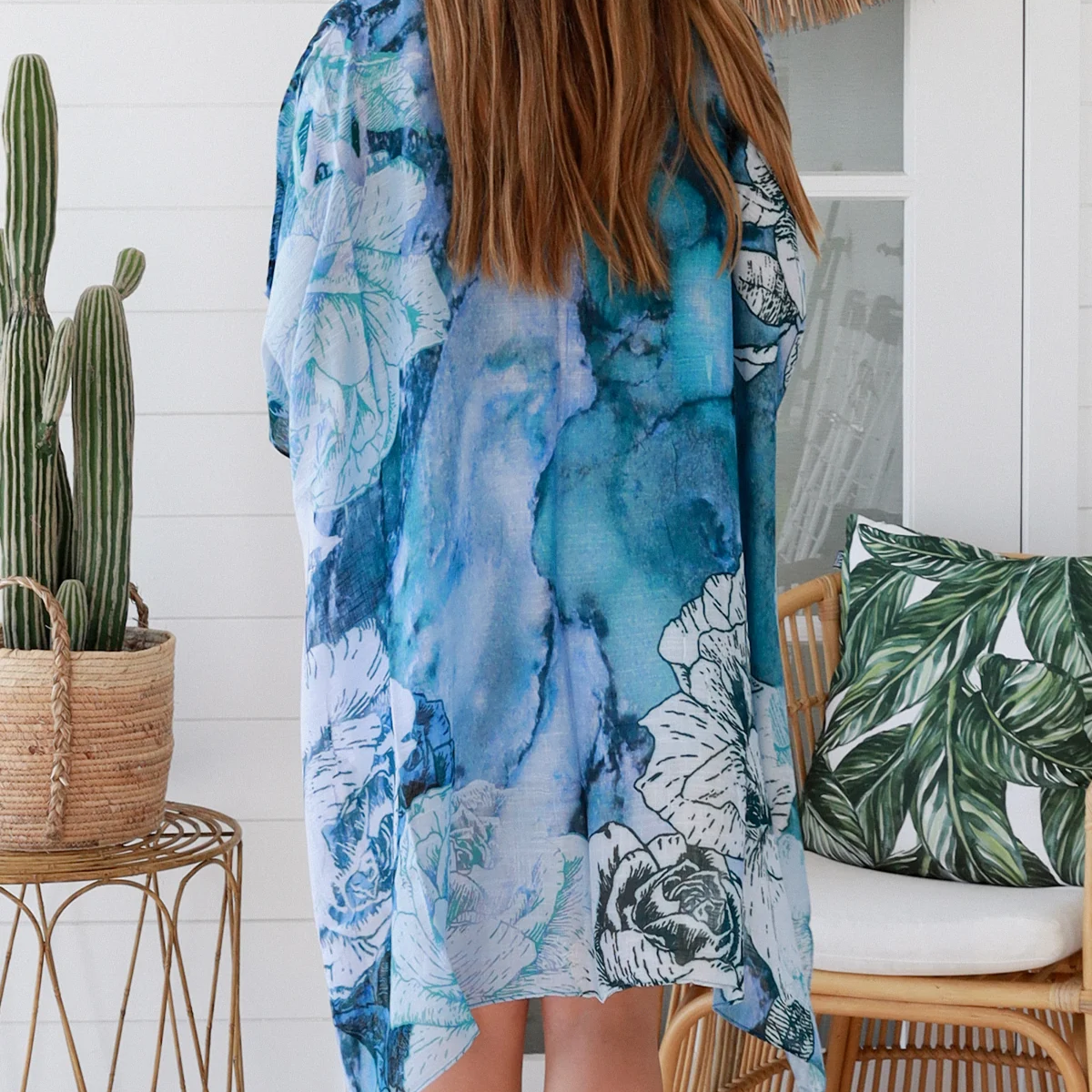 Person wearing a blue floral kimono standing in a room with a cactus plant and decorative pillows.