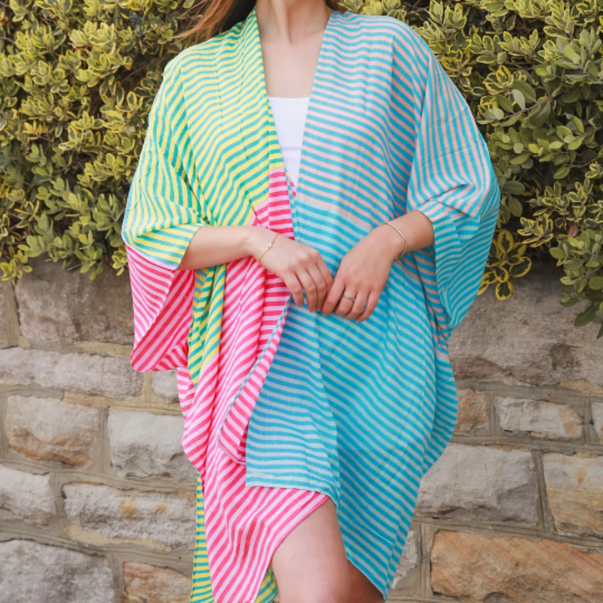 Woman wearing a colorful striped kimono against a stone wall and green foliage background