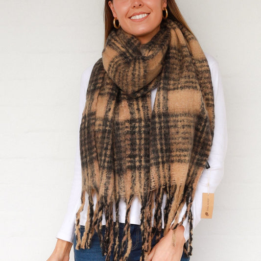 Woman wearing a brown plaid scarf with tassels on a plain background