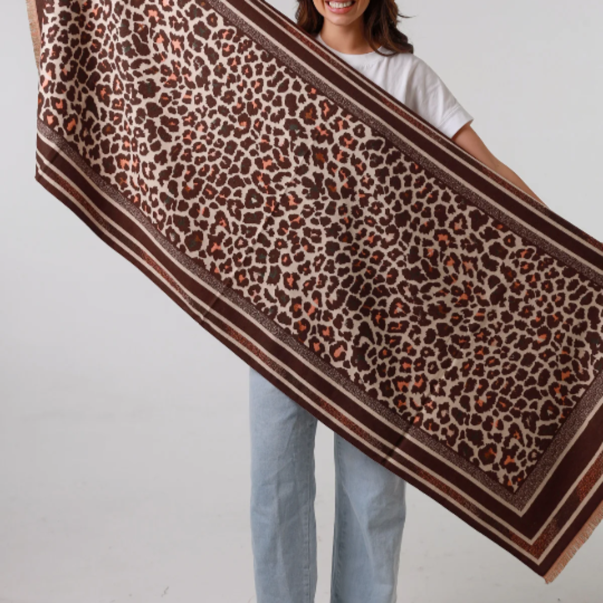 Woman holding a large leopard print scarf against a plain background