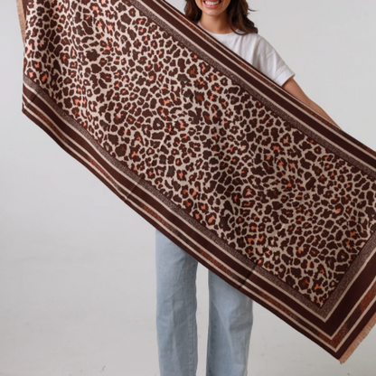 Woman holding a large leopard print scarf against a plain background