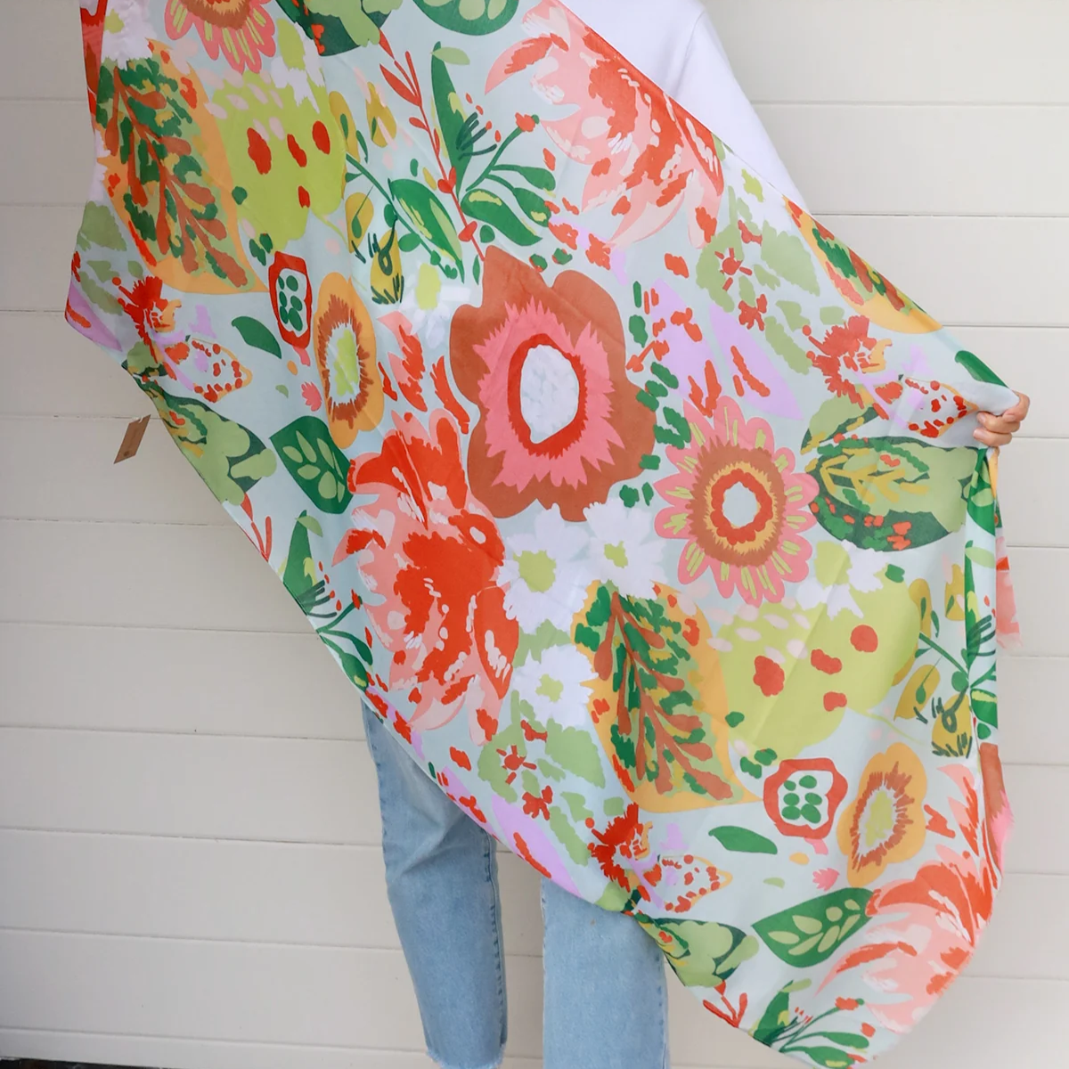 Woman holding a colorful floral scarf against a white wall.