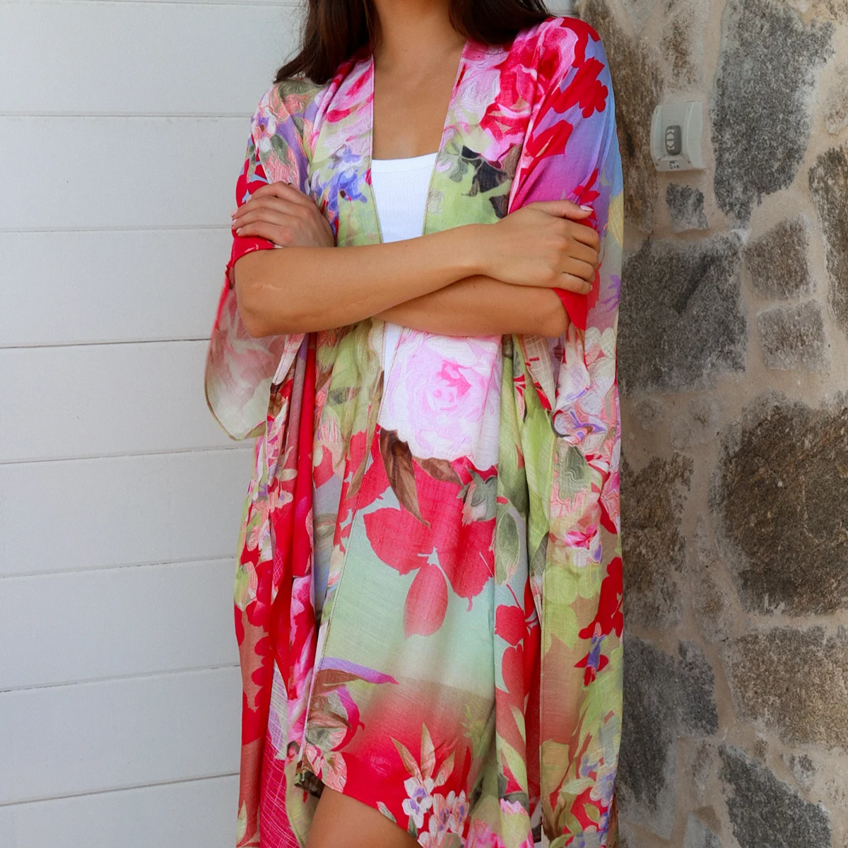Woman wearing a colorful floral kimono standing against a stone wall.