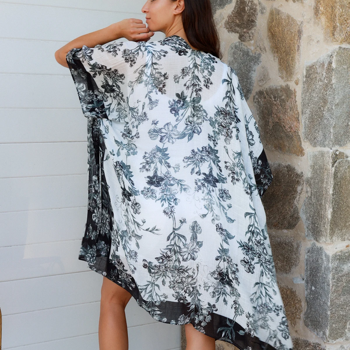 Woman wearing a floral kimono-style garment against a stone wall.