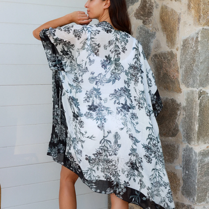 Woman wearing a floral kimono-style garment against a stone wall.