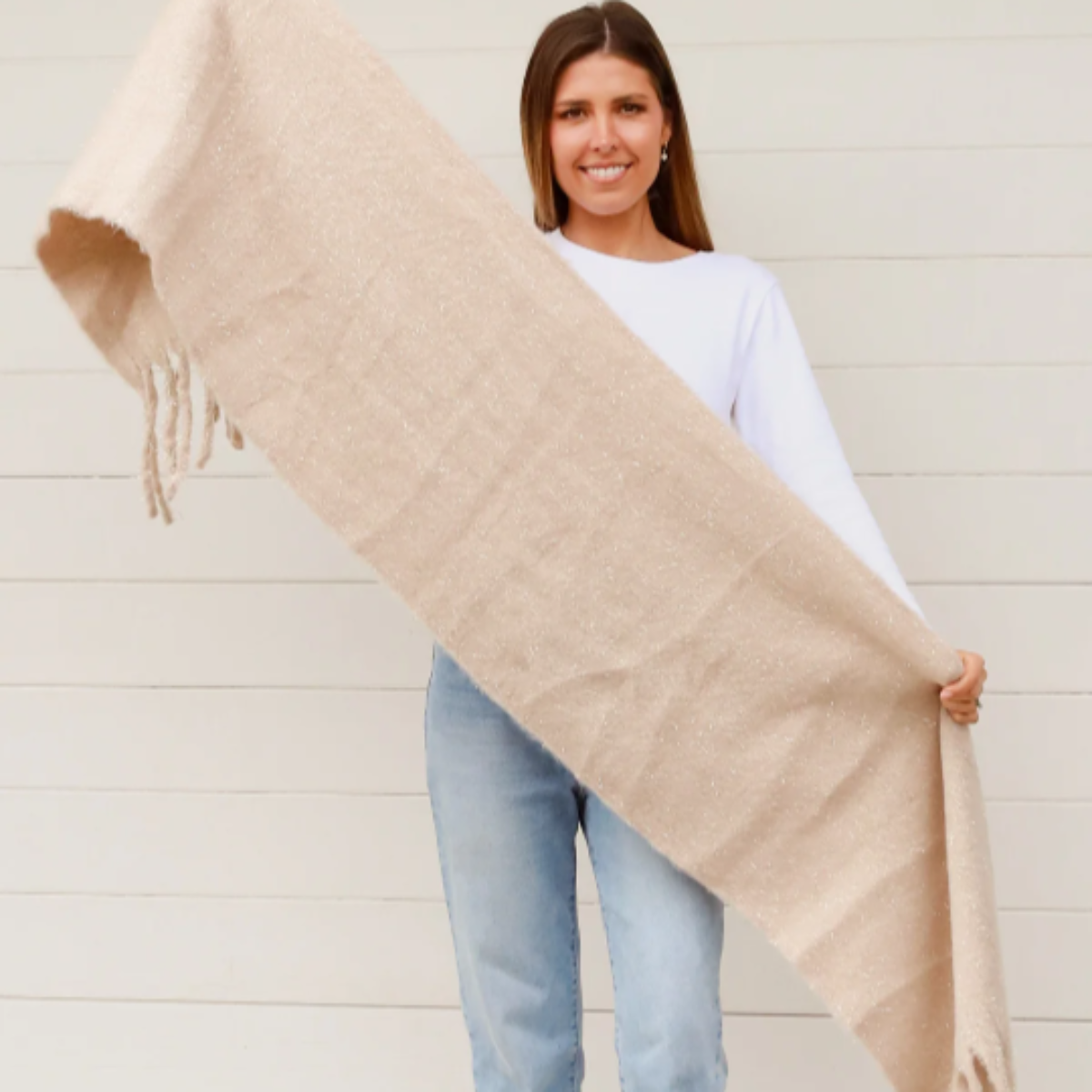 Woman holding a cream scarf against a white wall