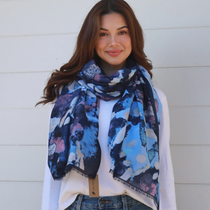 Woman wearing a colorful scarf and blue jeans against a white wall