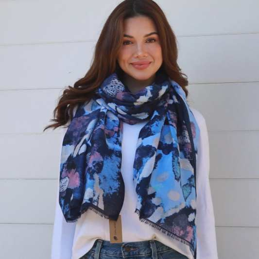 Woman wearing a colorful scarf and blue jeans against a white wall