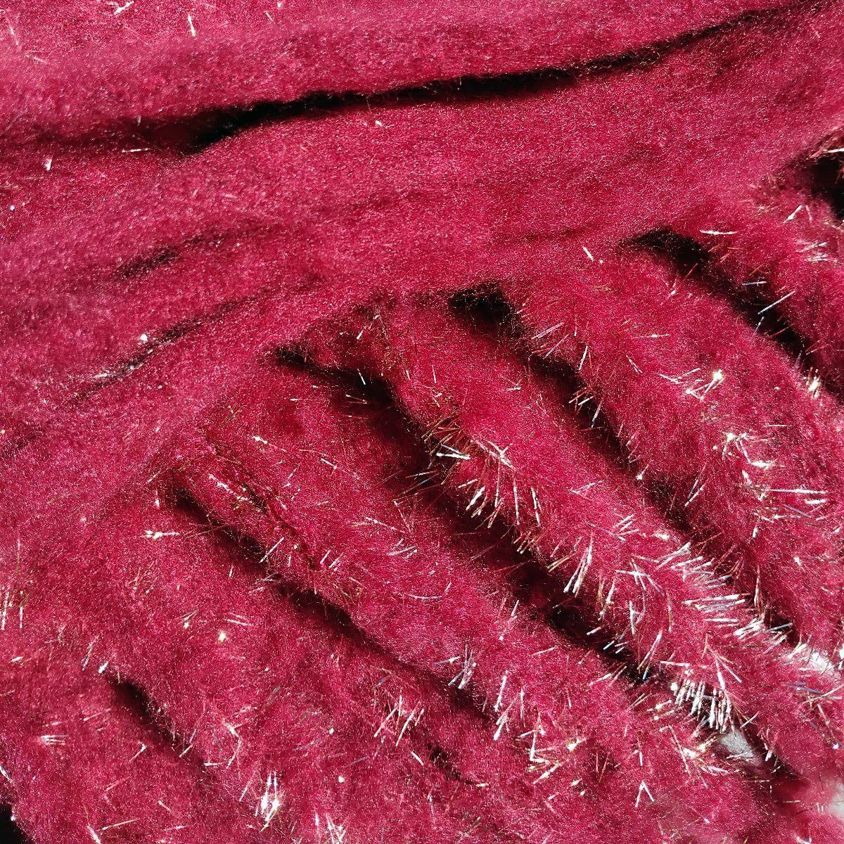 Close-up of a dark red scarf that is very soft and warm and has gold metallic fibres and  a chunky fringe