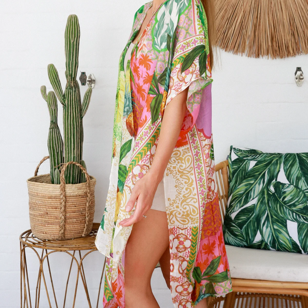 Woman wearing a colorful floral kimono standing in a room with a cactus plant and decorative pillows.