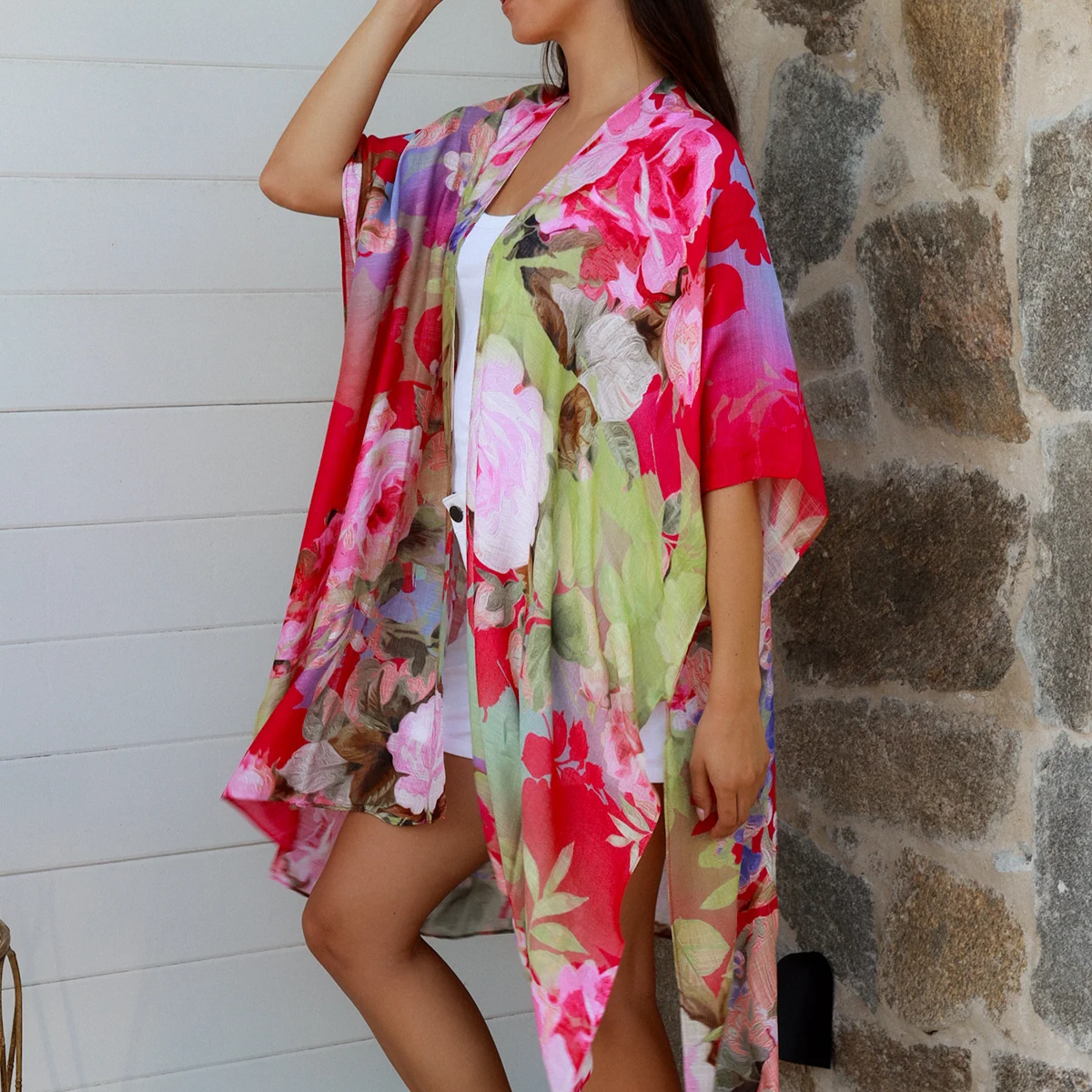 Woman wearing a colorful floral kimono standing against a stone wall.
