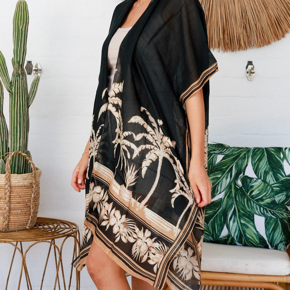 Woman wearing a black floral patterned cover-up in a tropical setting with a cactus and woven chair.