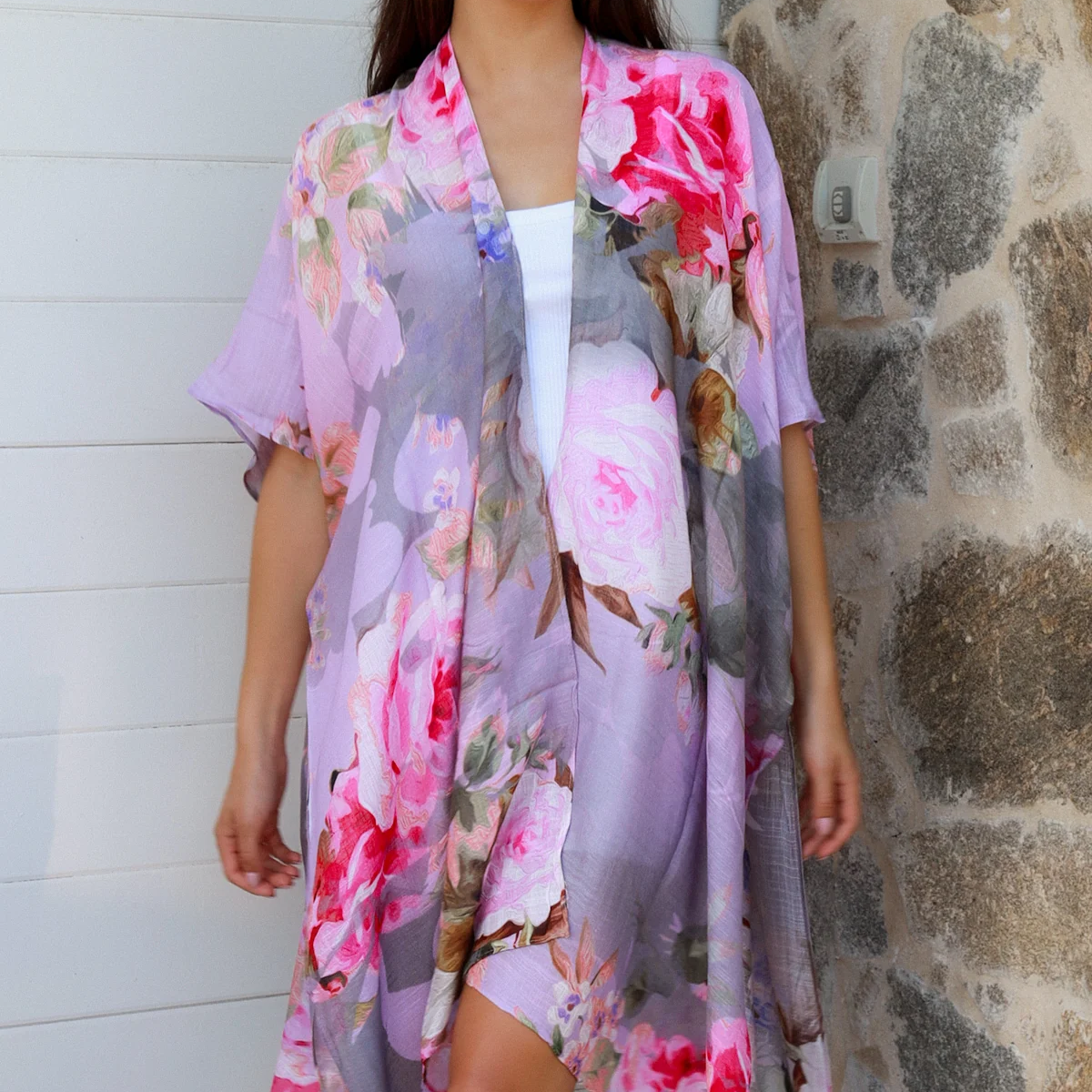 Woman wearing a floral kimono standing against a stone wall.