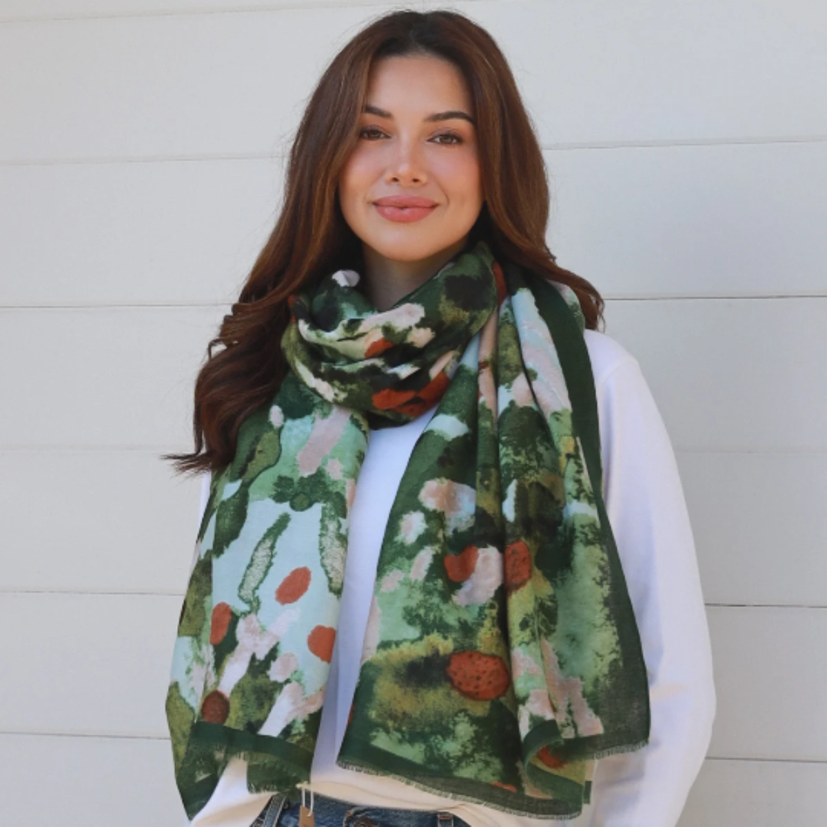 Woman wearing a green floral scarf, white shirt, and blue jeans against a white background