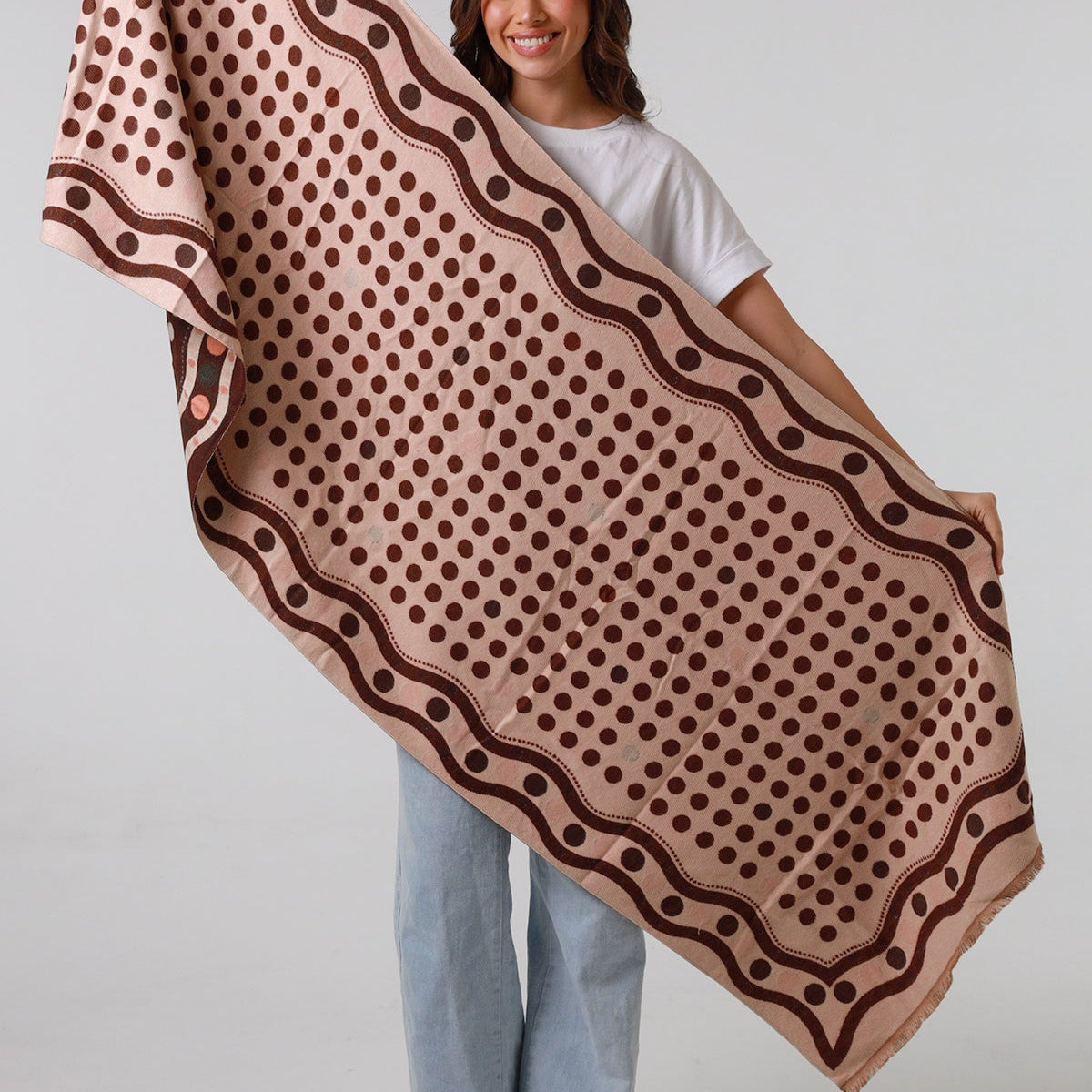Woman holding a large brown patterned scarf against a white background