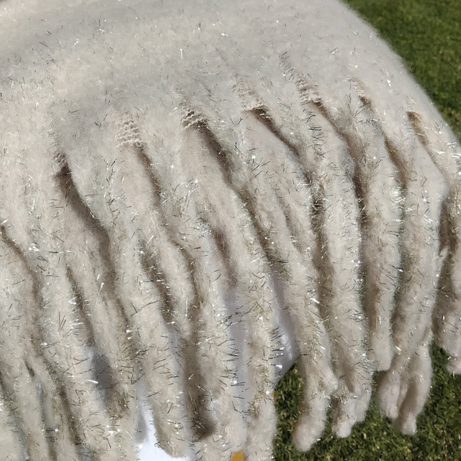 Close-up of a fluffy cream scarf with chunky tassels that is draped over a chair