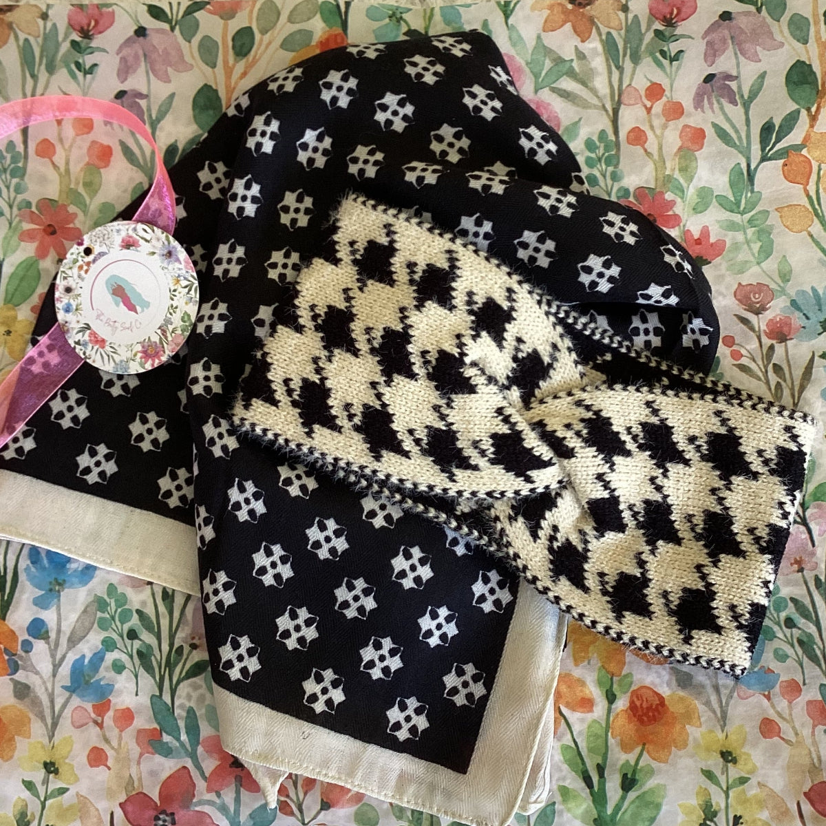 Knitted black and white patterned headband on a black scarf with a floral tissue paper background