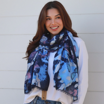 Woman wearing a blue floral scarf, white shirt, and jeans against a light background