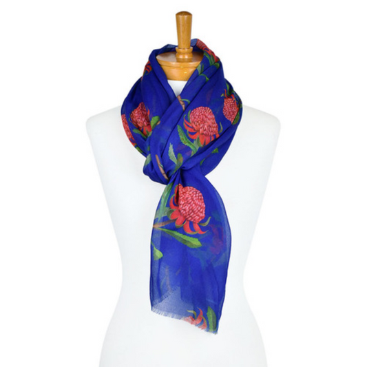 a lightweight cotton scarf that has a navy blue background and bright pink Waratah flowers with green stems and leaves. The scarf is tied around a mannequin.