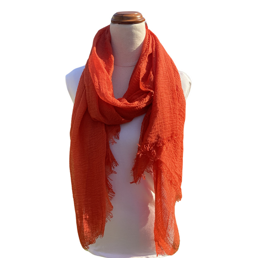 a mannequin wearing a plain dark orange coloured scarf. The scarf has a textured weave and a frayed edge on all sides.