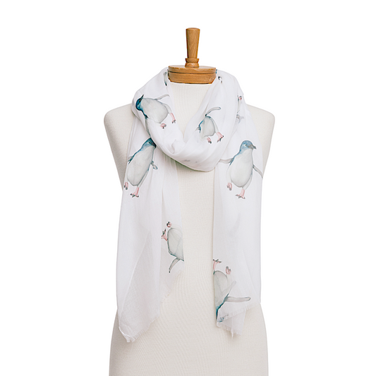 a cute ladies scarf that has a plain white background and cute penguins, finished with a frayed edge.