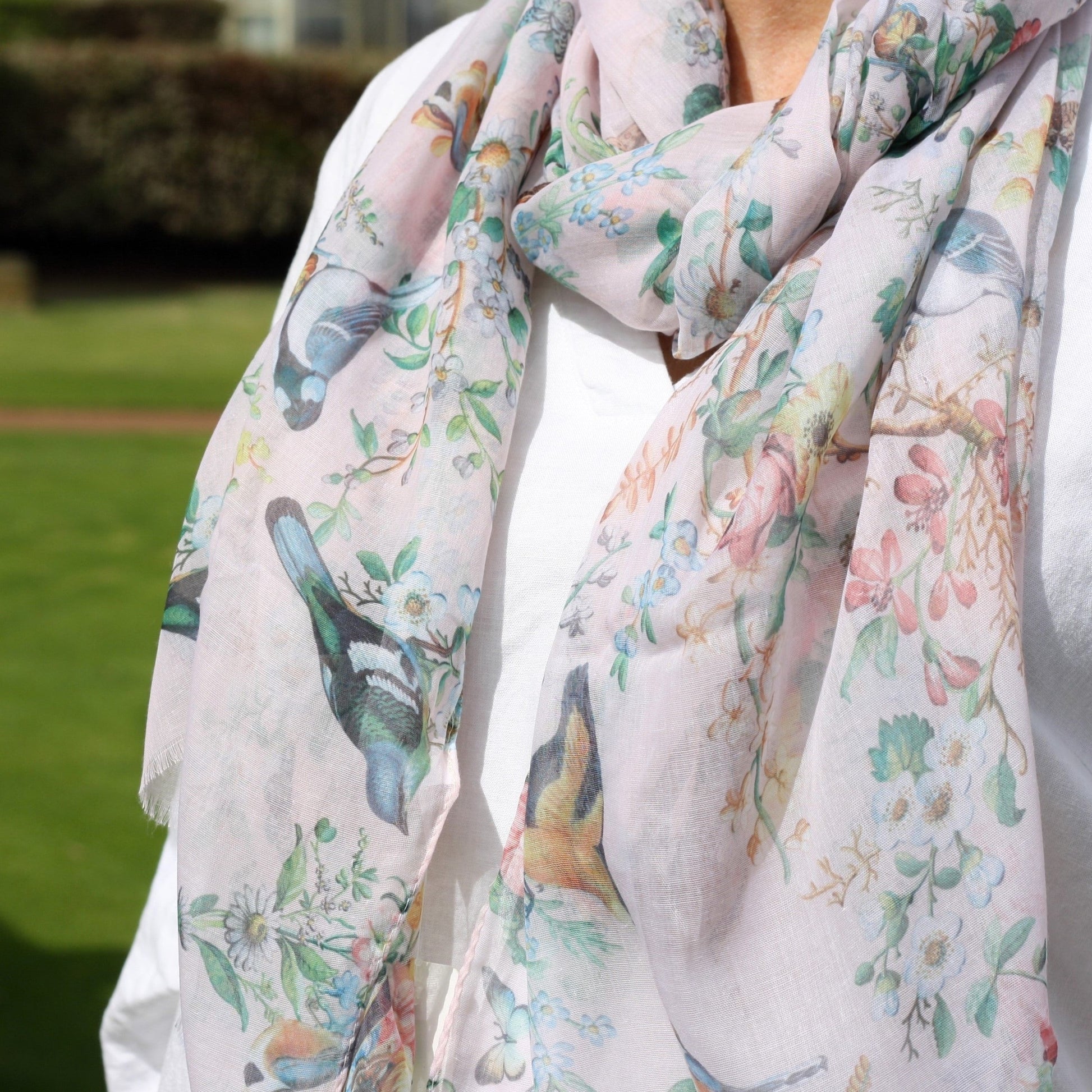 a close up view of a pale pink ladies scarf that has birds, pretty flowers and butterflies