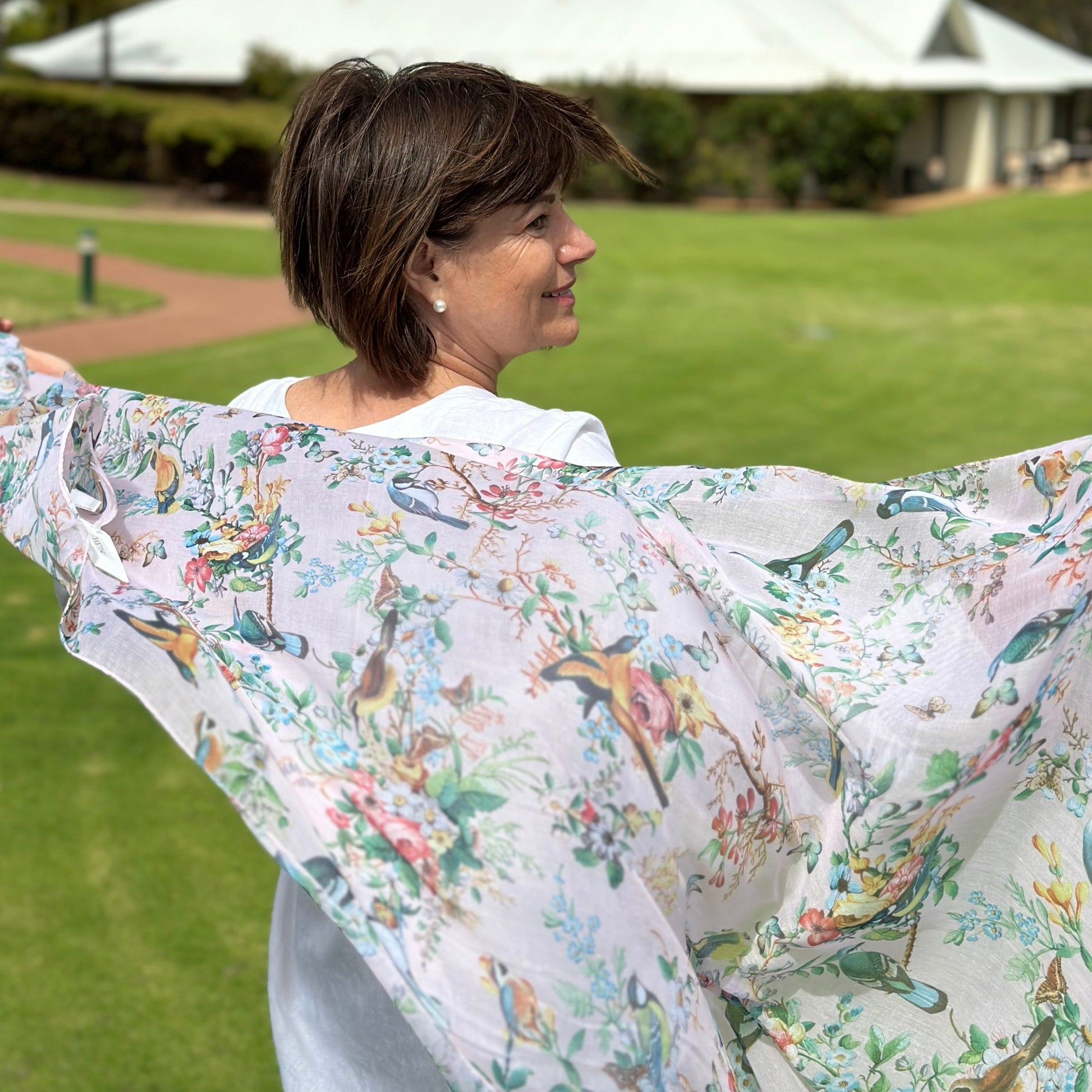 a lady holding a pale pink scarf that has pretty birds, flowers and butterflies