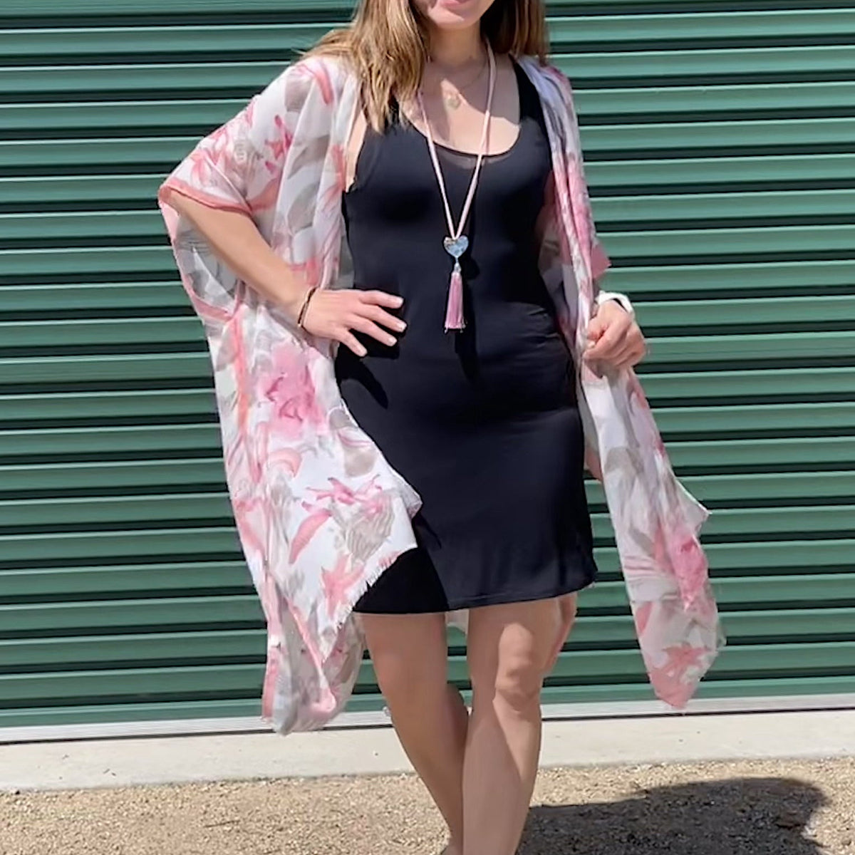 Woman wearing a black dress and floral kimono against a green background