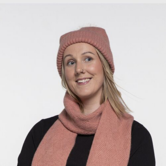 Woman wearing a pink knit beanie and scarf on a white background