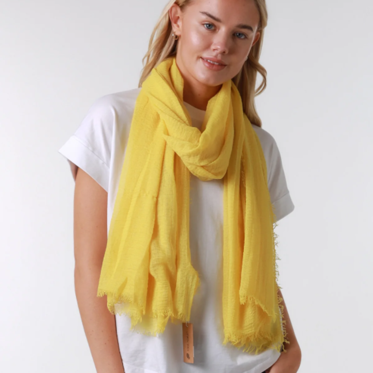 Woman wearing a yellow scarf, white t-shirt, and blue jeans on a white background