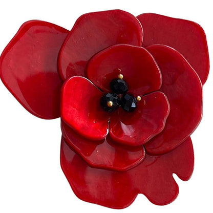 A glossy red poppy flower brooch with a black beaded center and tiny gold accents, shown on a plain white background.