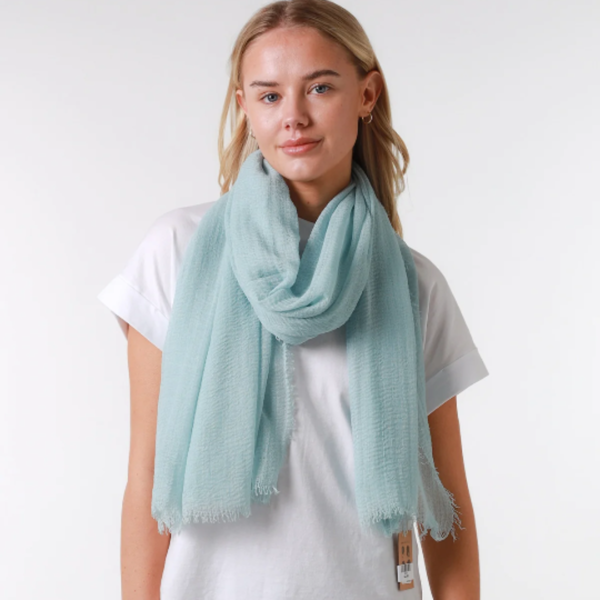 Person wearing a light blue scarf, white t-shirt, and dark jeans on a plain background