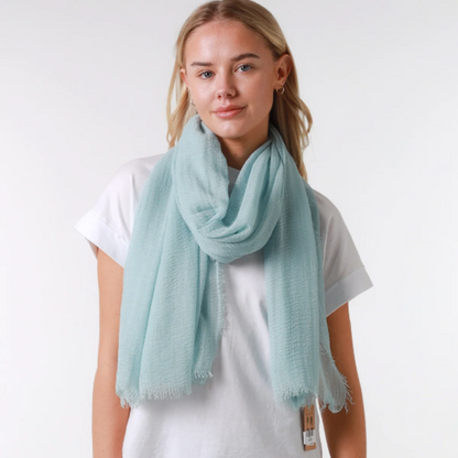 Person wearing a light blue scarf, white t-shirt, and dark jeans on a plain background