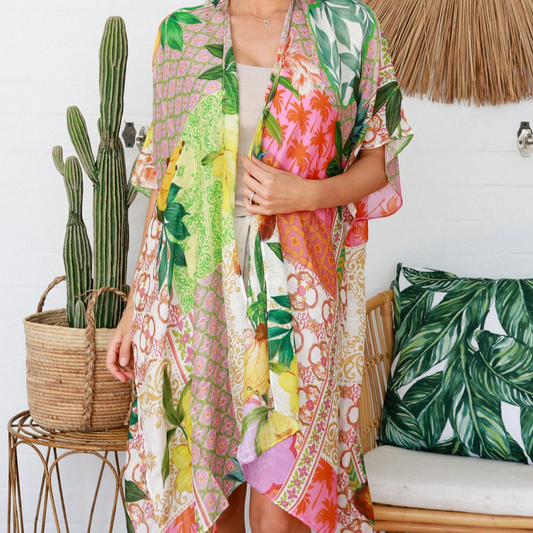 Woman wearing a colorful floral kimono in a tropical setting with a cactus and woven chair.