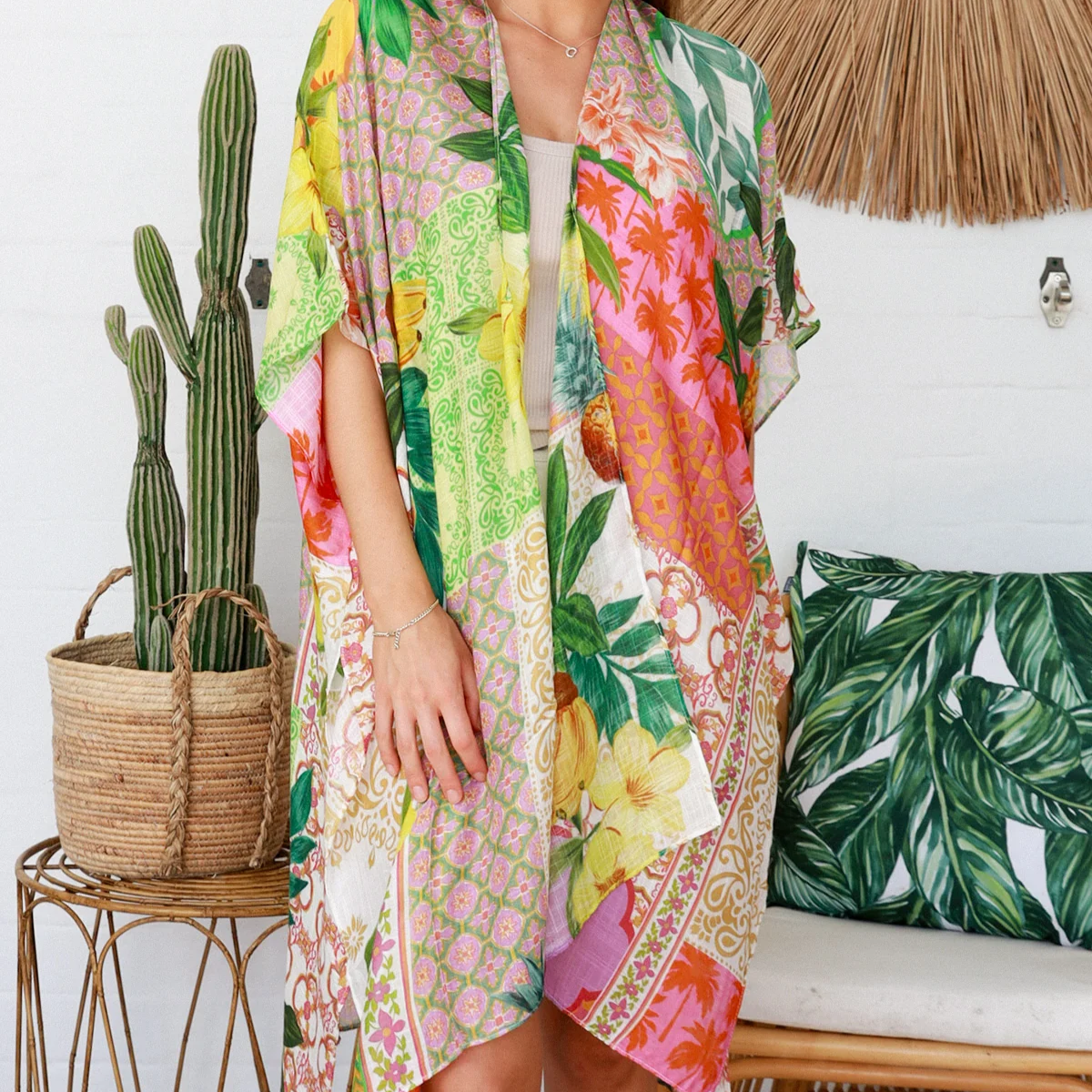 Woman wearing a colorful floral kimono standing in a room with a cactus plant and decorative pillows.
