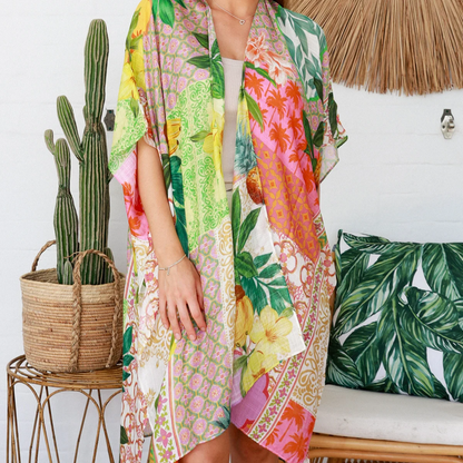 Woman wearing a colorful floral kimono standing in a room with a cactus plant and decorative pillows.