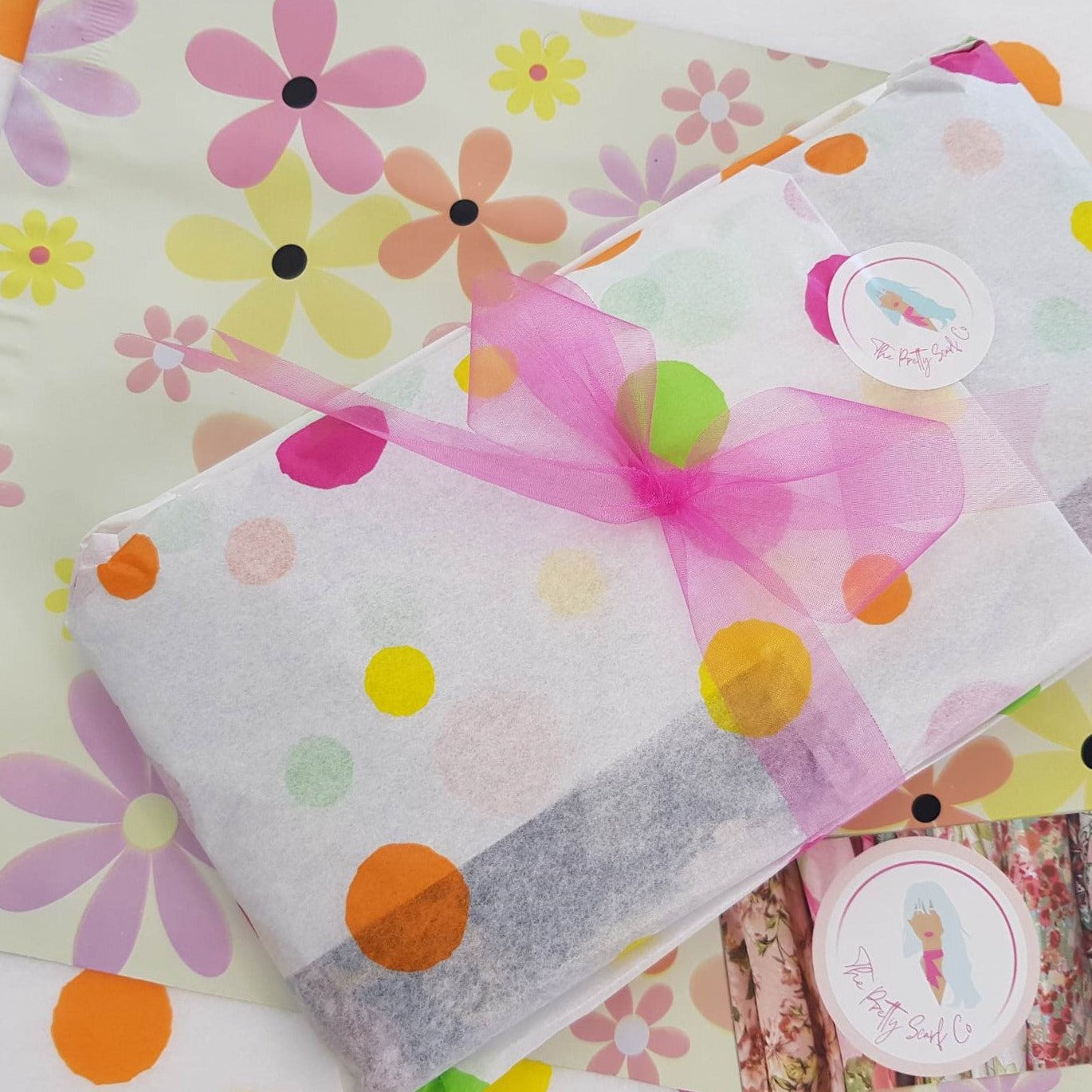 a ladies scarf gift wrapped in white tissue paper with pastel coloured spots and tied with a bright pink ribbon