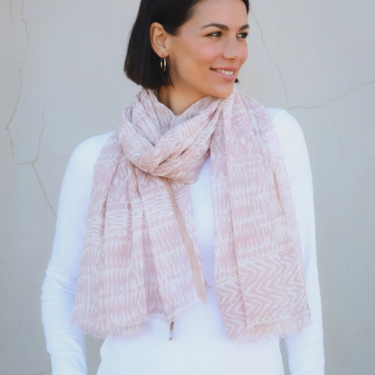 Woman wearing a light taupe brown scarf against a plain background
