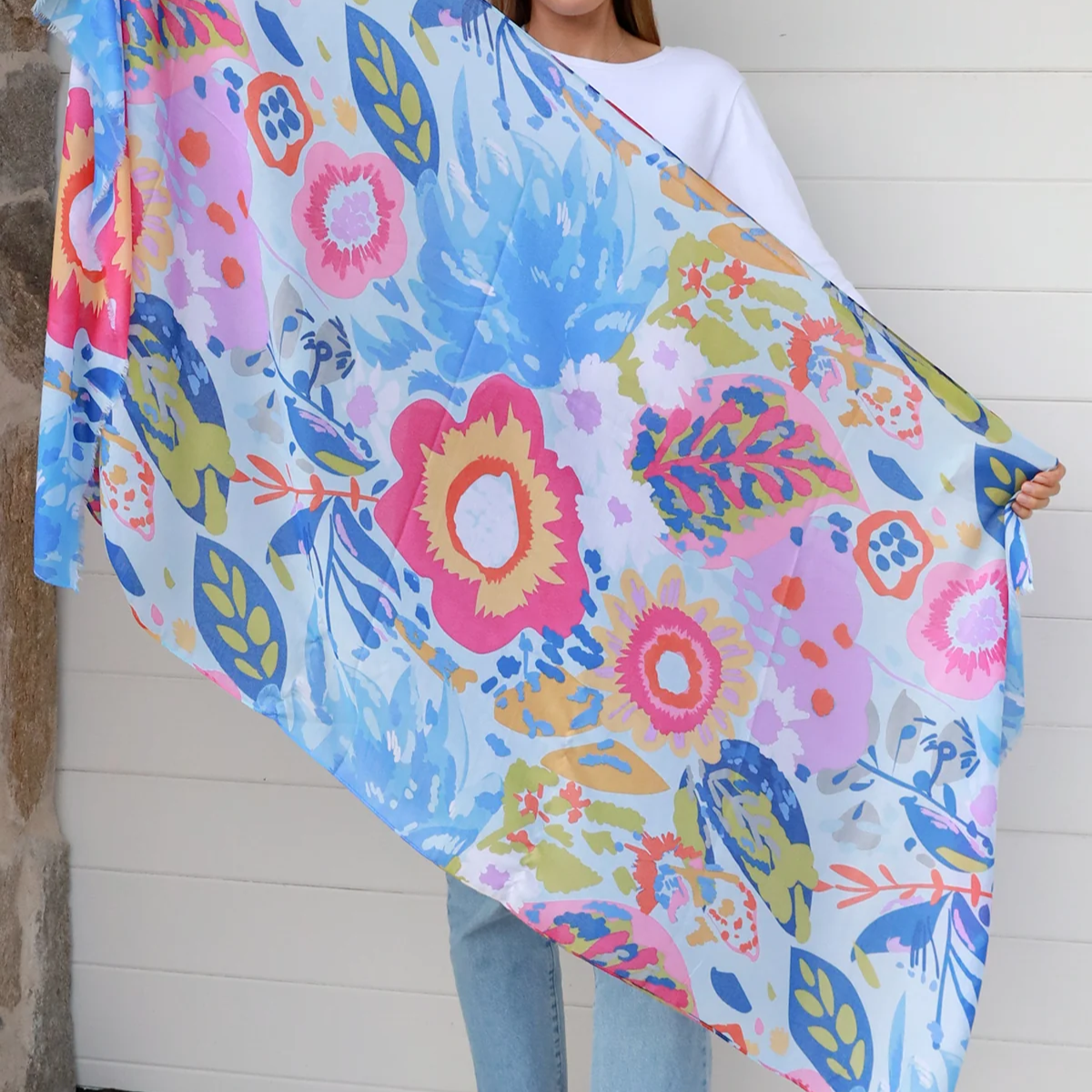 Woman holding a blue colorful floral blanket against a white wall.