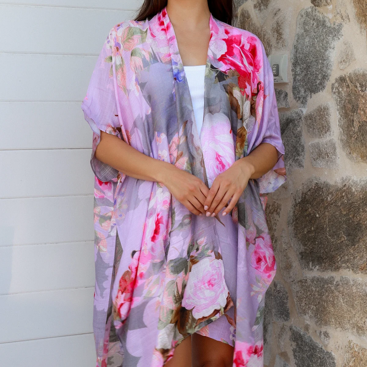 Woman wearing a floral kimono standing against a stone wall.