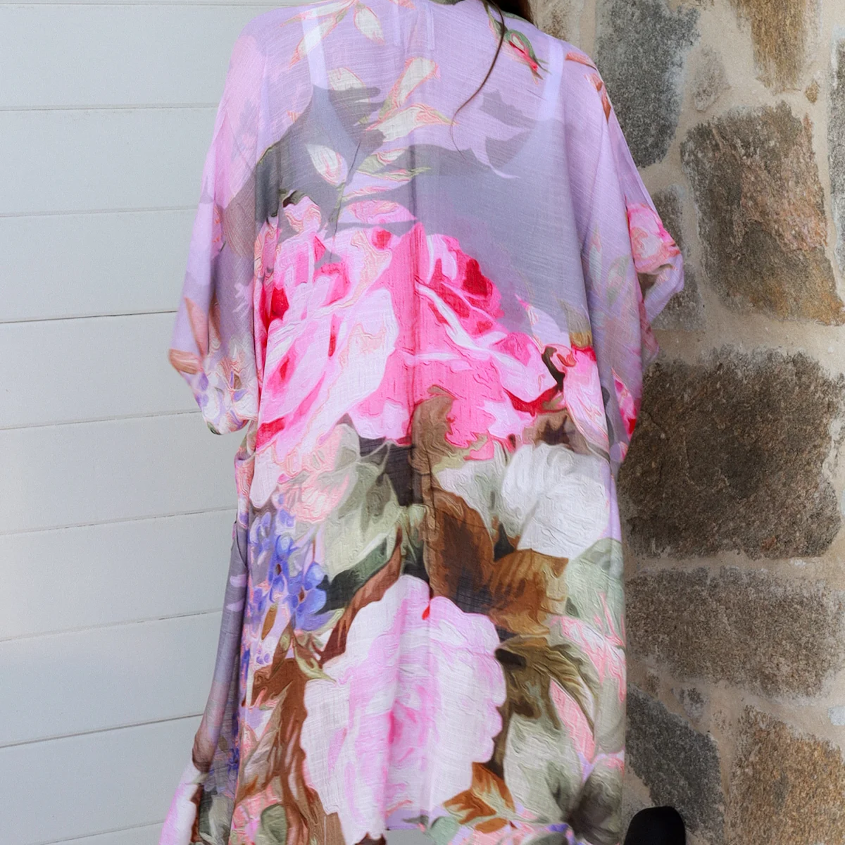 Woman wearing a floral kimono-style garment against a stone wall.